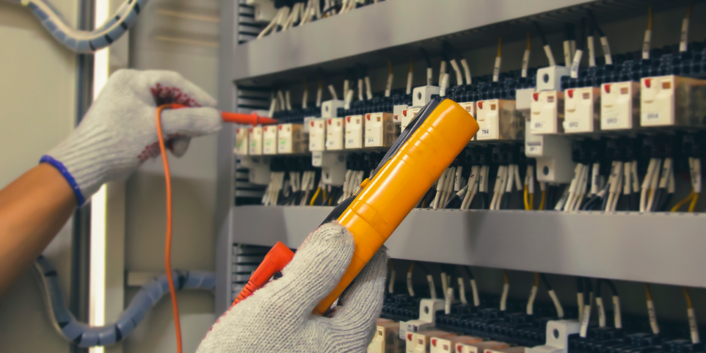 An Great Lakes Electric technician testing a commercial breaker panel with a multimeter.