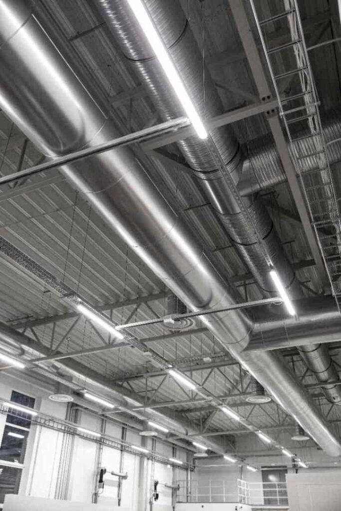 LED strip lights run alongside ductwork across a warehouse ceiling, showcasing a commercial LED lighting installation by Great Lakes Electric.